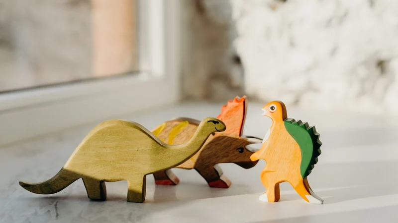 Trzy drewniane figurki dinozaurów na parapecie w ciepłym świetle