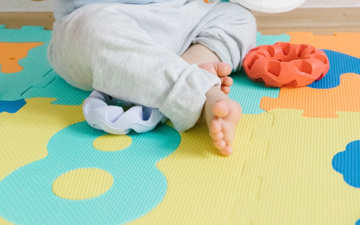 Kolorowa piankowa mata puzzlowa z cyframi, na niej stopy dziecka i zabawki