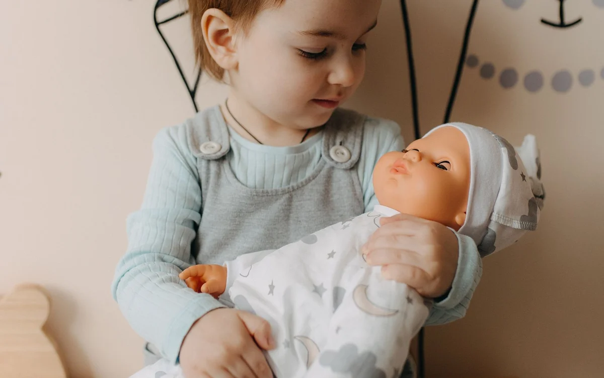 Małe dziecko czule tuli lalkę-bobasa w kocyku