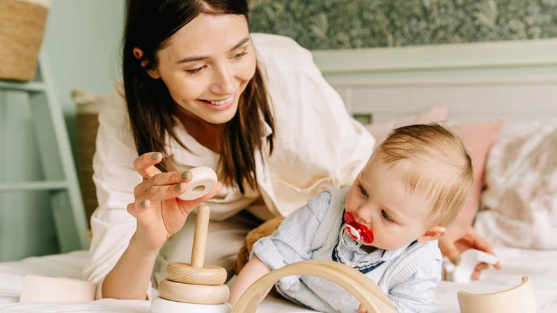 Uśmiechnięta mama pokazuje niemowlęciu drewnianą piramidkę z krążkami