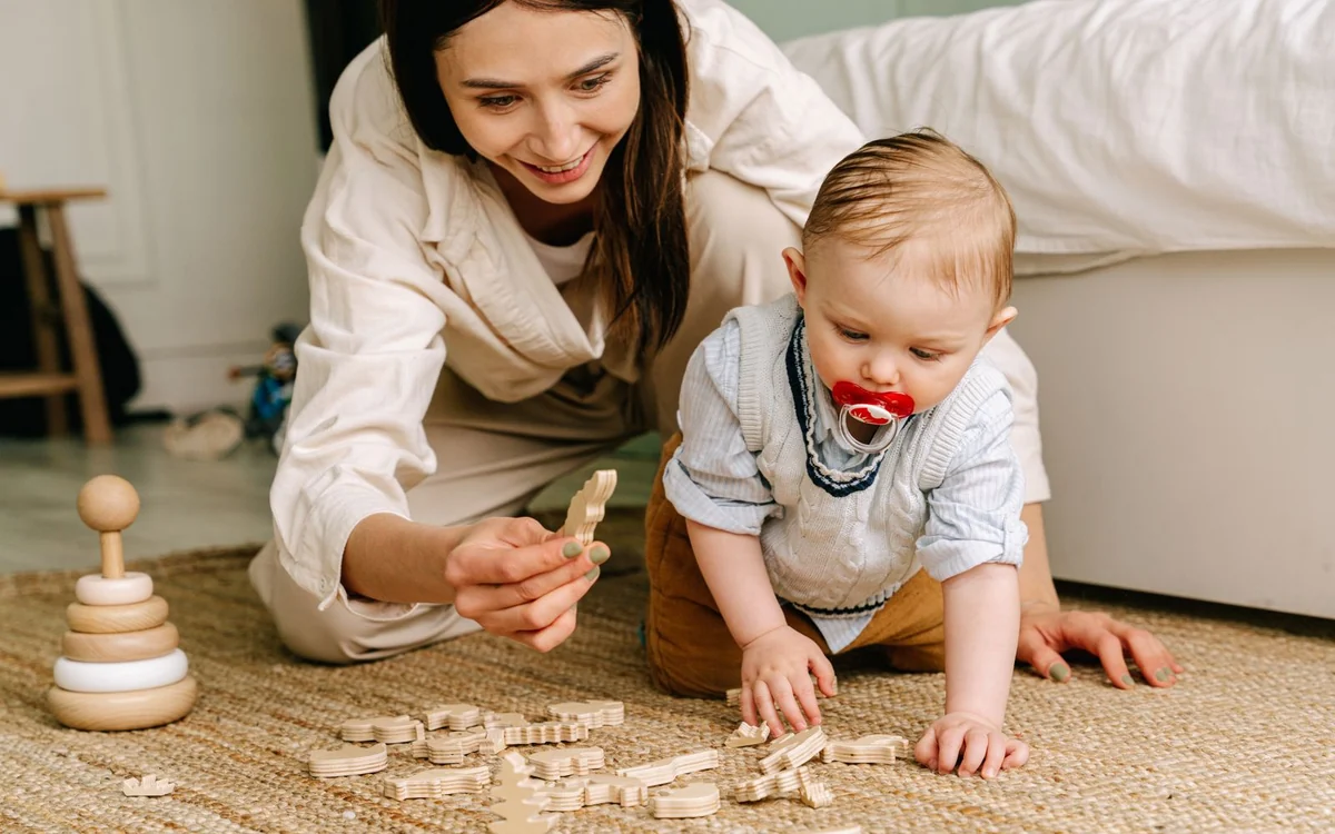 Mama i niemowlę bawią się drewnianymi elementami na jutowym dywanie