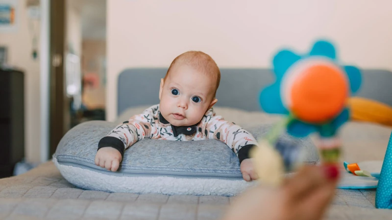 Niemowlę na brzuszku unosi głowę, opierając się o poduszkę do tummy time