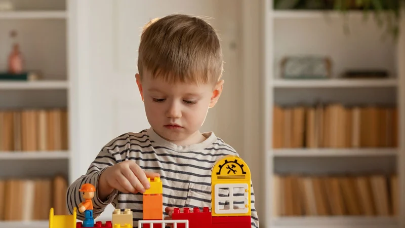 Czterolatek skupiony buduje z klocków przy stole w domu